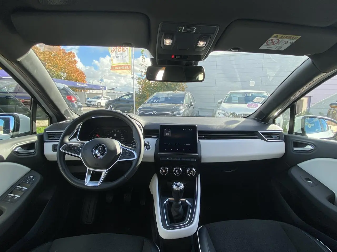 Vue intérieure avant de la Renault Clio blanche 2021, tableau de bord moderne avec écran tactile et volant multifonction.