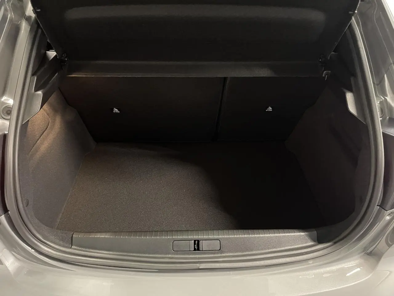 Coffre ouvert vu de face, intérieur noir, carrosserie gris selenium métallisée visible autour de l'ouverture.