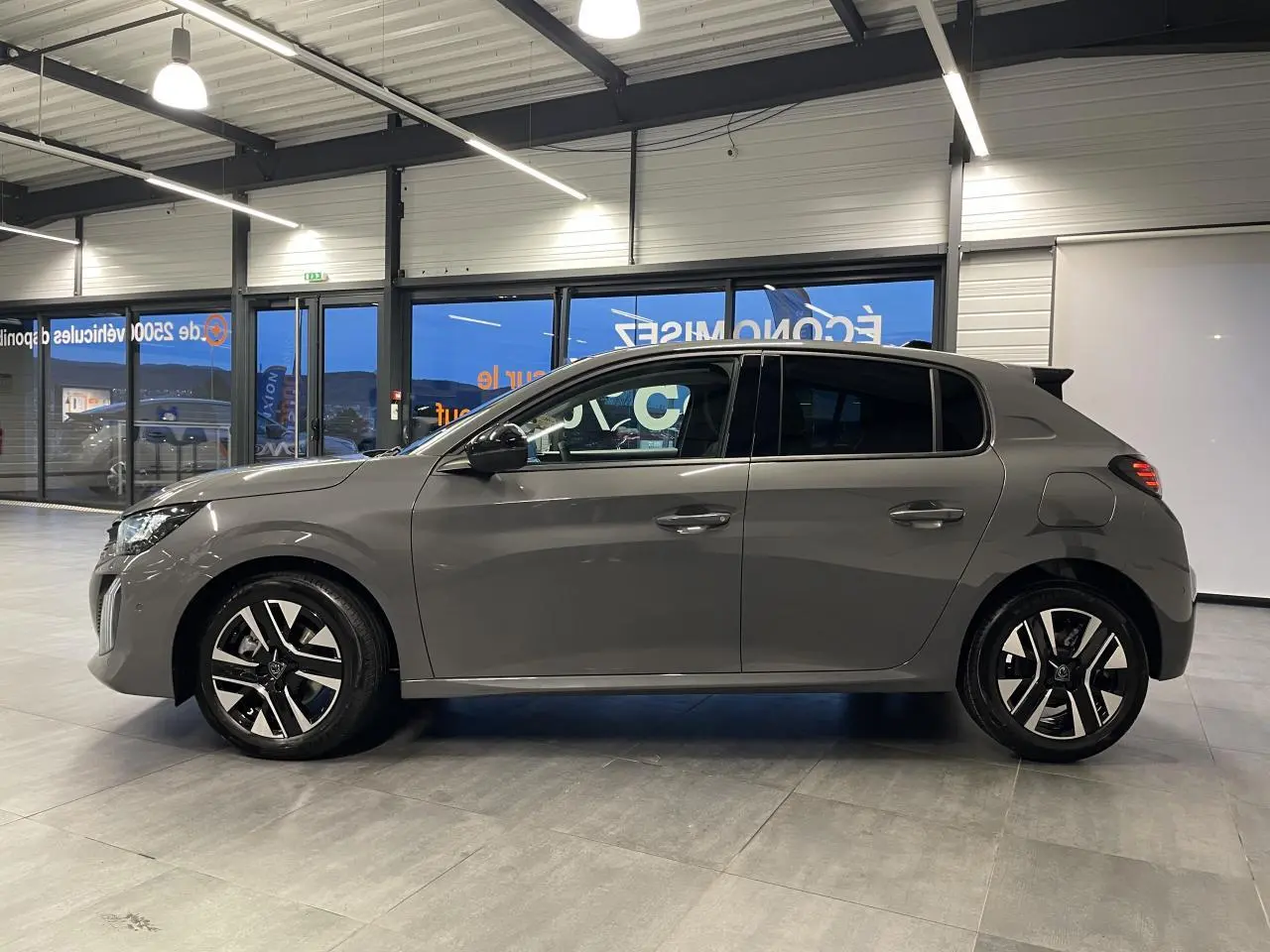 Peugeot 208 gris selenium vue de profil côté gauche, jantes alliage bi-tons et poignées couleur carrosserie.