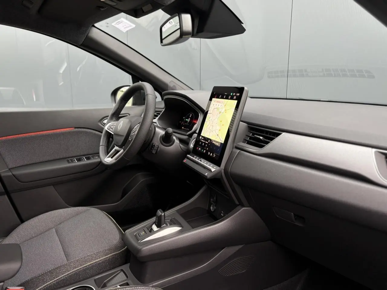 Vue intérieure côté conducteur du Renault Captur 2025, tableau de bord noir avec écran tactile vertical et volant multifonction.