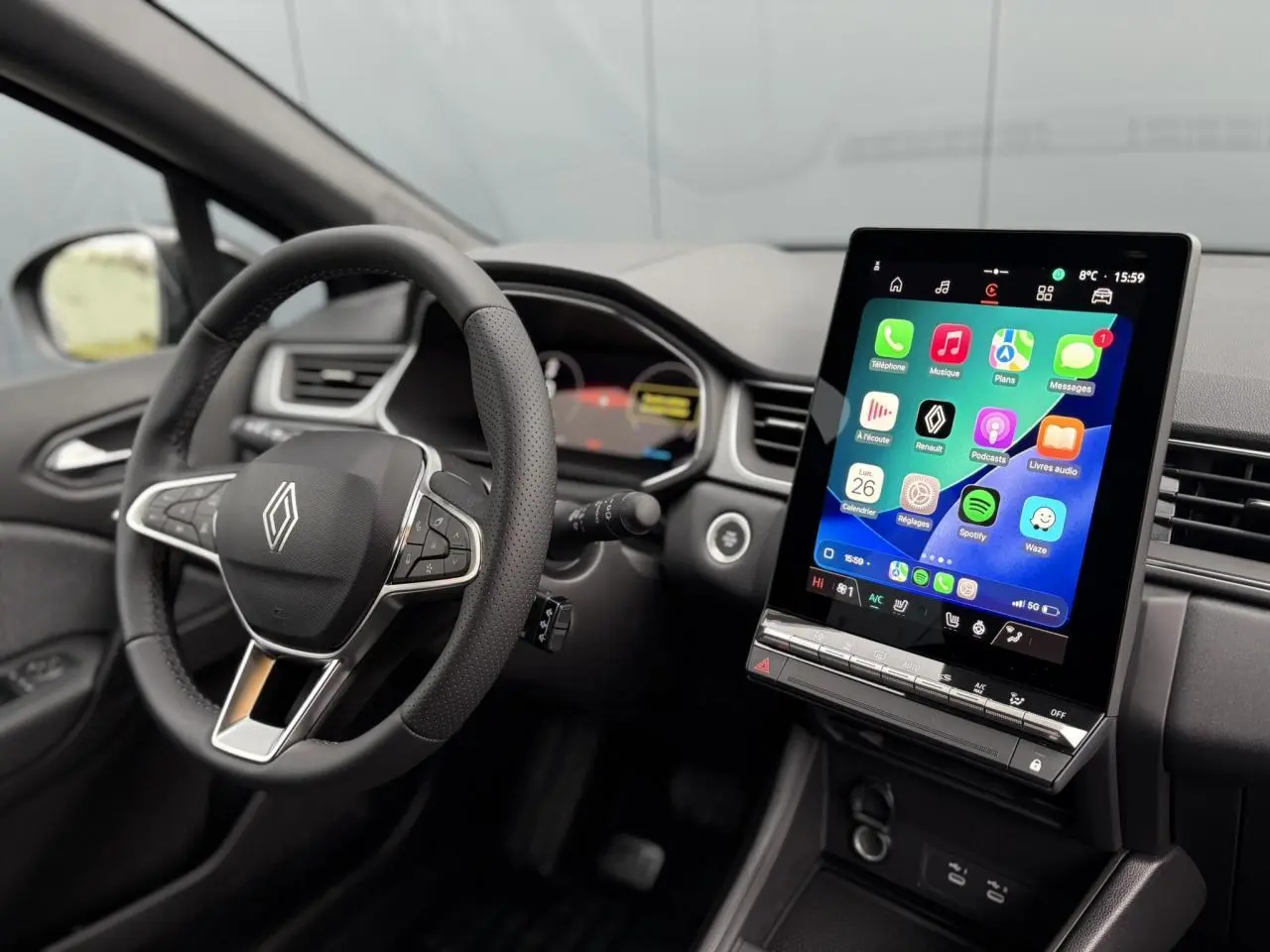 Vue intérieure côté conducteur du Renault Captur 2025, volant noir avec logo Renault et grand écran tactile central allumé.