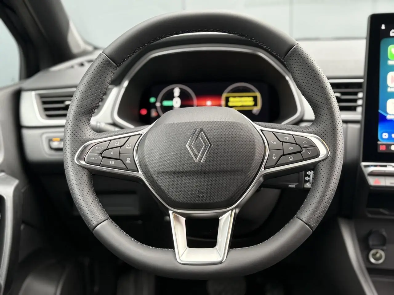 Vue rapprochée du volant noir perforé avec commandes intégrées du Renault Captur 2025, tableau de bord numérique en arrière-plan.