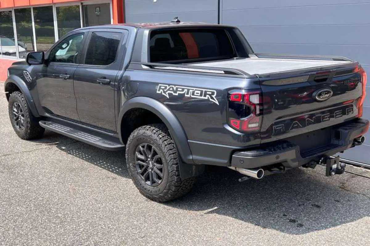Vue 3/4 arrière droite du Ford Ranger Raptor gris météore avec logo Raptor et roues tout-terrain.