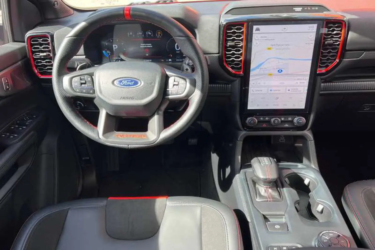 Vue intérieure avant du Ford Ranger Raptor 2025, volant cuir noir avec surpiqûres rouges et écran tactile vertical.