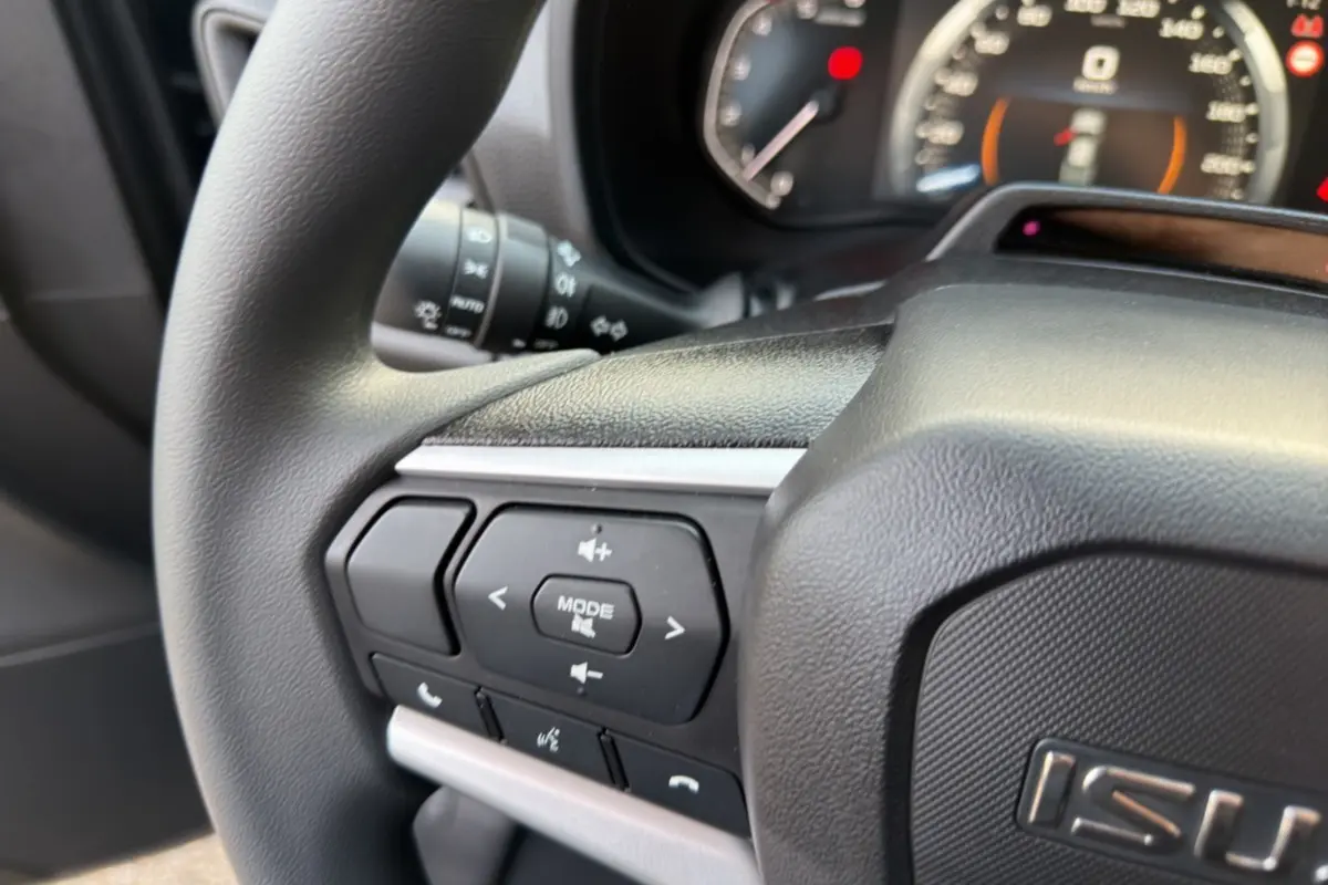 Gros plan sur le volant multifonctions noir du pick-up Isuzu D-MAX 2026 avec commandes audio et téléphone intégrées.