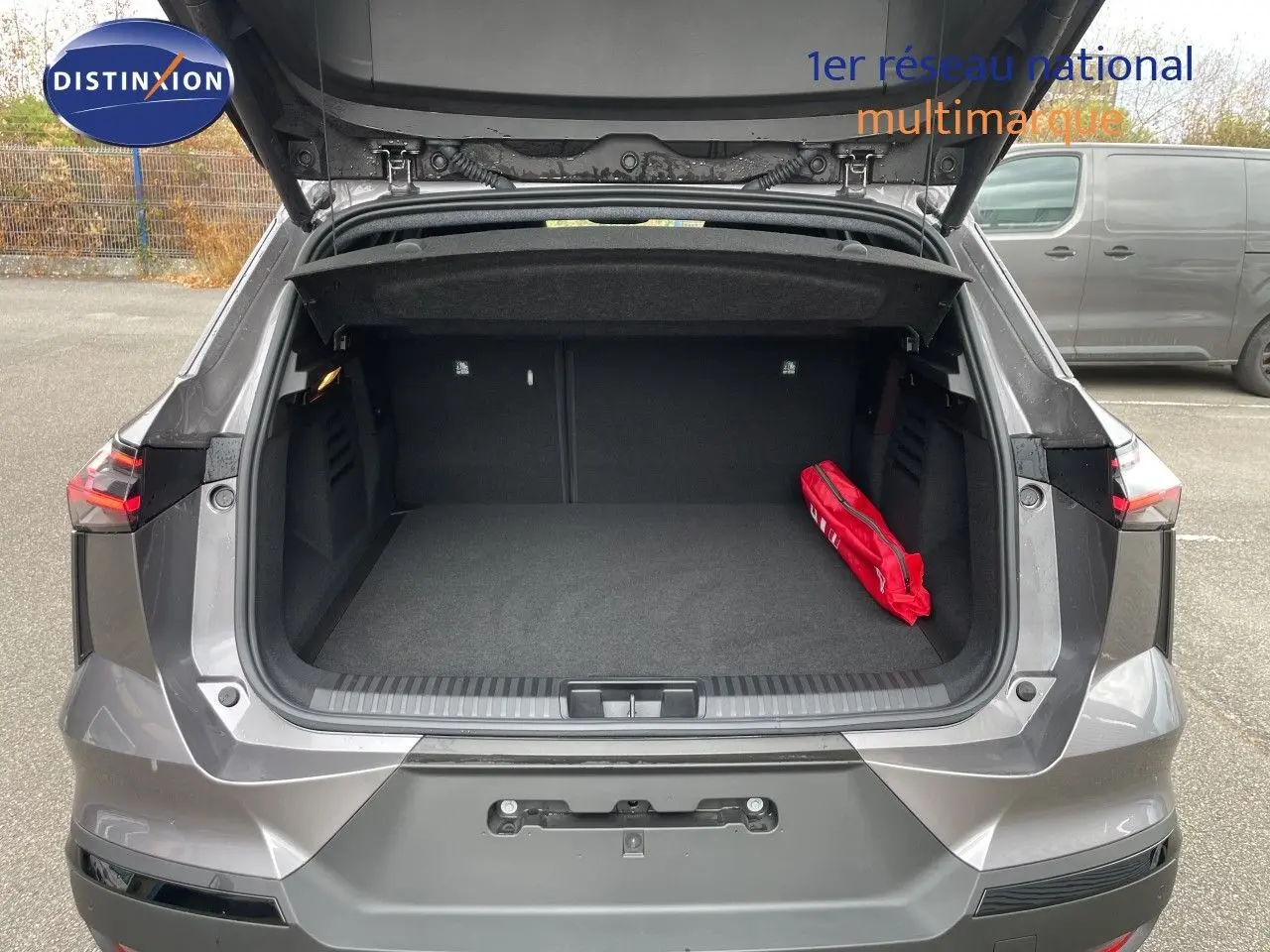 Coffre ouvert vu de l'arrière d'une Renault Symbioz gris cassiopée métal avec un kit de sécurité rouge à l'intérieur.