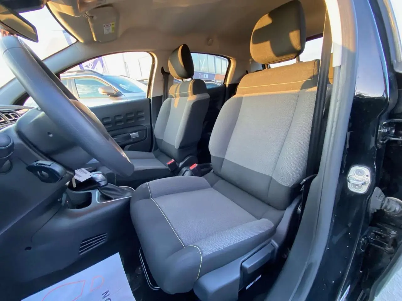 Vue intérieure côté conducteur de la Citroën C3 Shine 2023 avec sièges tissu gris et noir, volant et tableau de bord visibles.