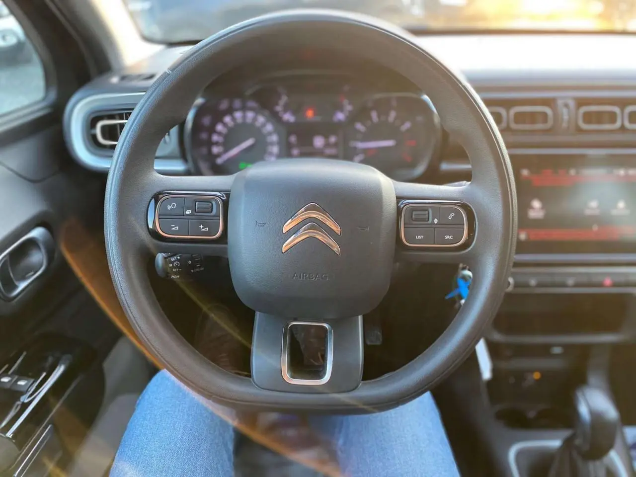 Vue intérieure centrée sur le volant Citroën C3 Shine 2023 avec commandes audio et tableau de bord éclairé.