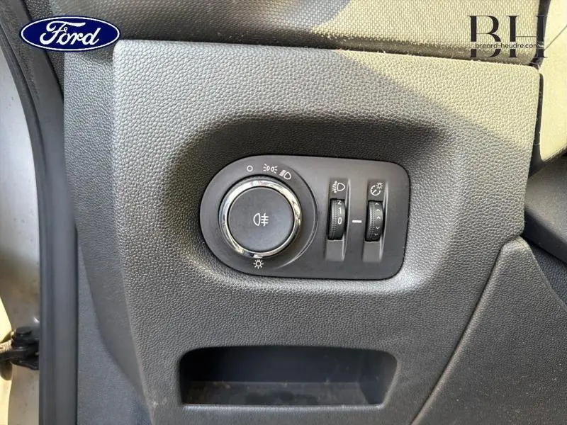 Gros plan sur les commandes d'éclairage noires à gauche du tableau de bord d'une Opel Corsa gris minéral 2014.