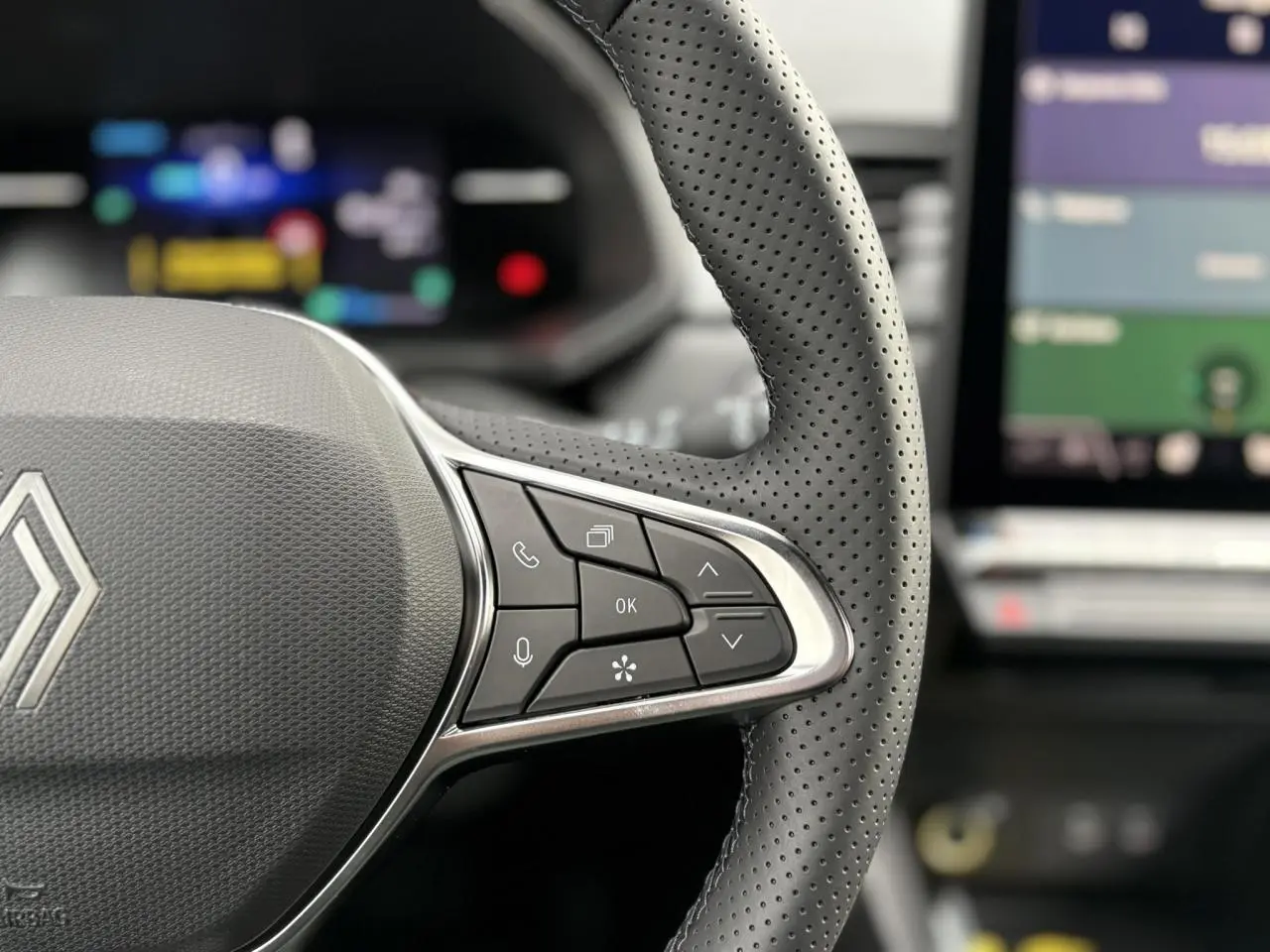 Gros plan sur le volant perforé noir du Renault Captur 2025 avec commandes intégrées et écran numérique flou en arrière-plan.