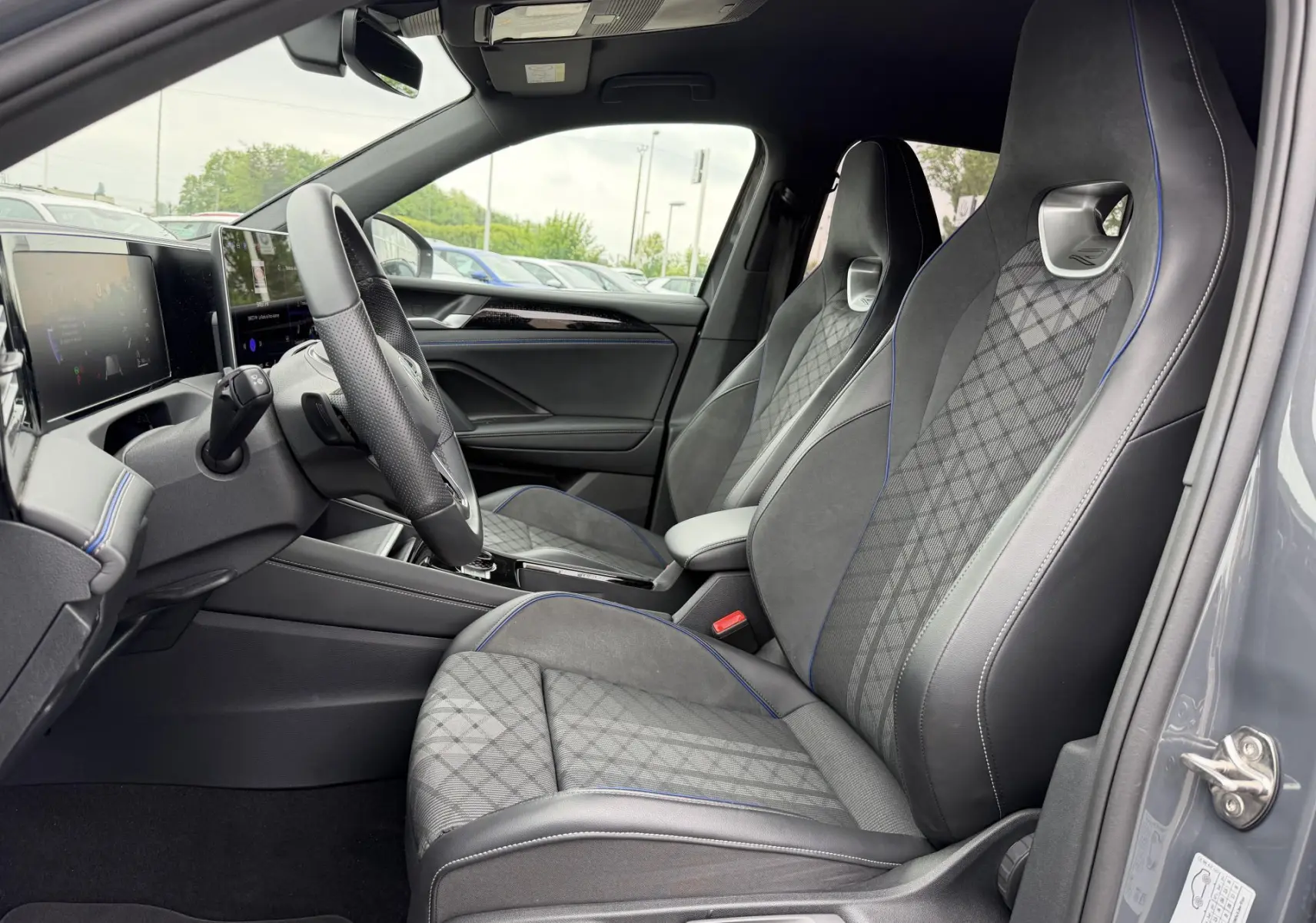 Vue intérieure côté conducteur du Volkswagen Tiguan gris 2025, sièges sport en tissu et cuir avec surpiqûres bleues.