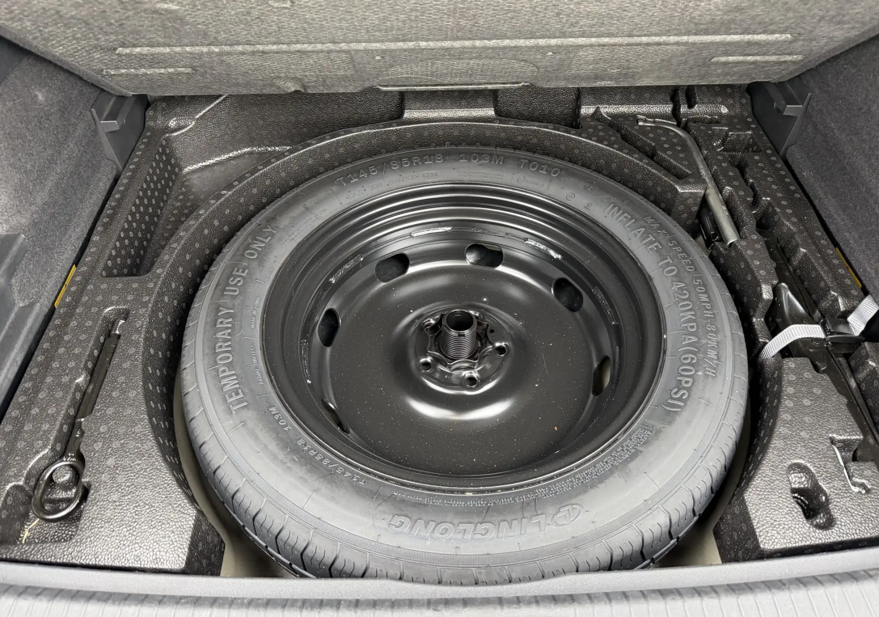Vue plongeante sur la roue de secours compacte noire dans le coffre du Volkswagen Tiguan gris 2025.