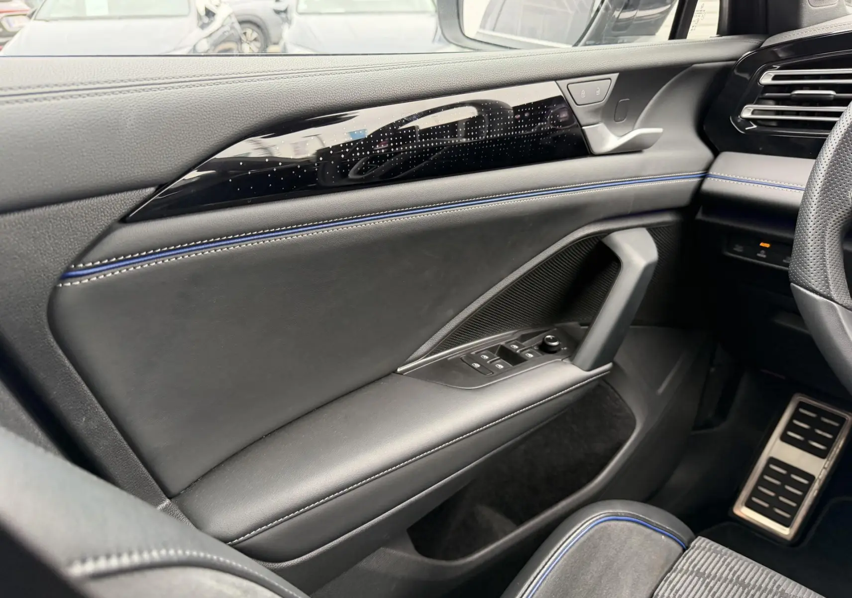 Détail de la porte avant gauche du Volkswagen Tiguan 2025, intérieur noir avec surpiqûres bleues et inserts brillants.