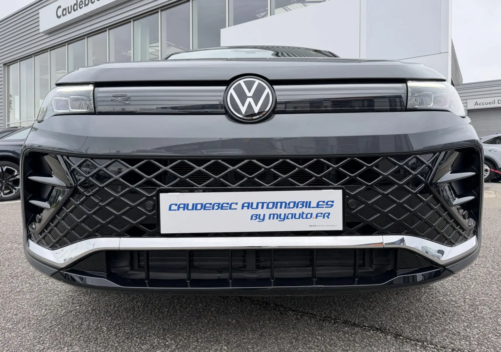 Vue frontale rapprochée du Volkswagen Tiguan gris 2025 avec calandre noire en losange et logo VW lumineux.