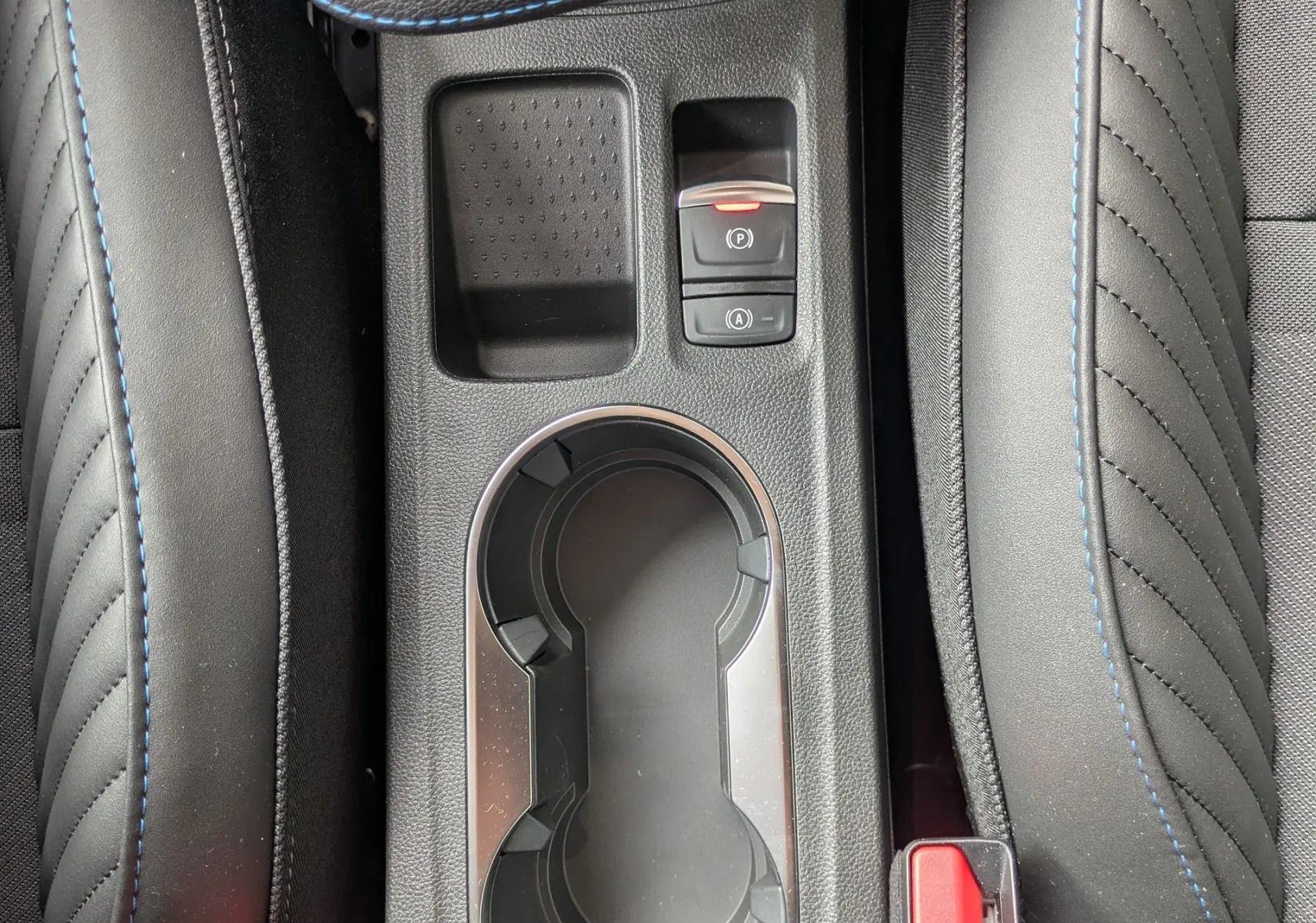 Vue plongeante sur la console centrale noire avec porte-gobelets et boutons de frein à main et auto-hold du Renault Symbioz gris Rafale.
