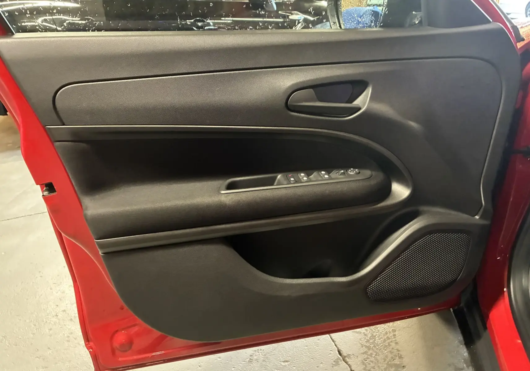 Vue intérieure de la porte avant gauche rouge de la Fiat 600 1.2 Hybrid 2024 avec commandes de vitres et haut-parleur intégré.