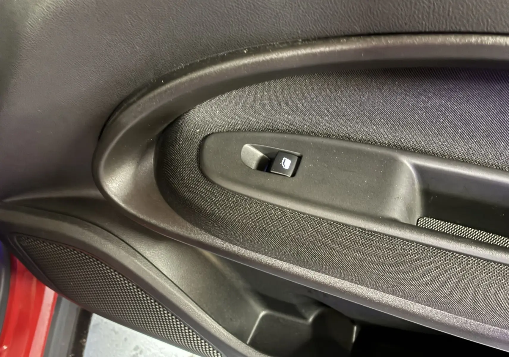 Gros plan sur la commande de lève-vitre noir intégrée à la porte côté gauche d’une FIAT 600 rouge 2024.