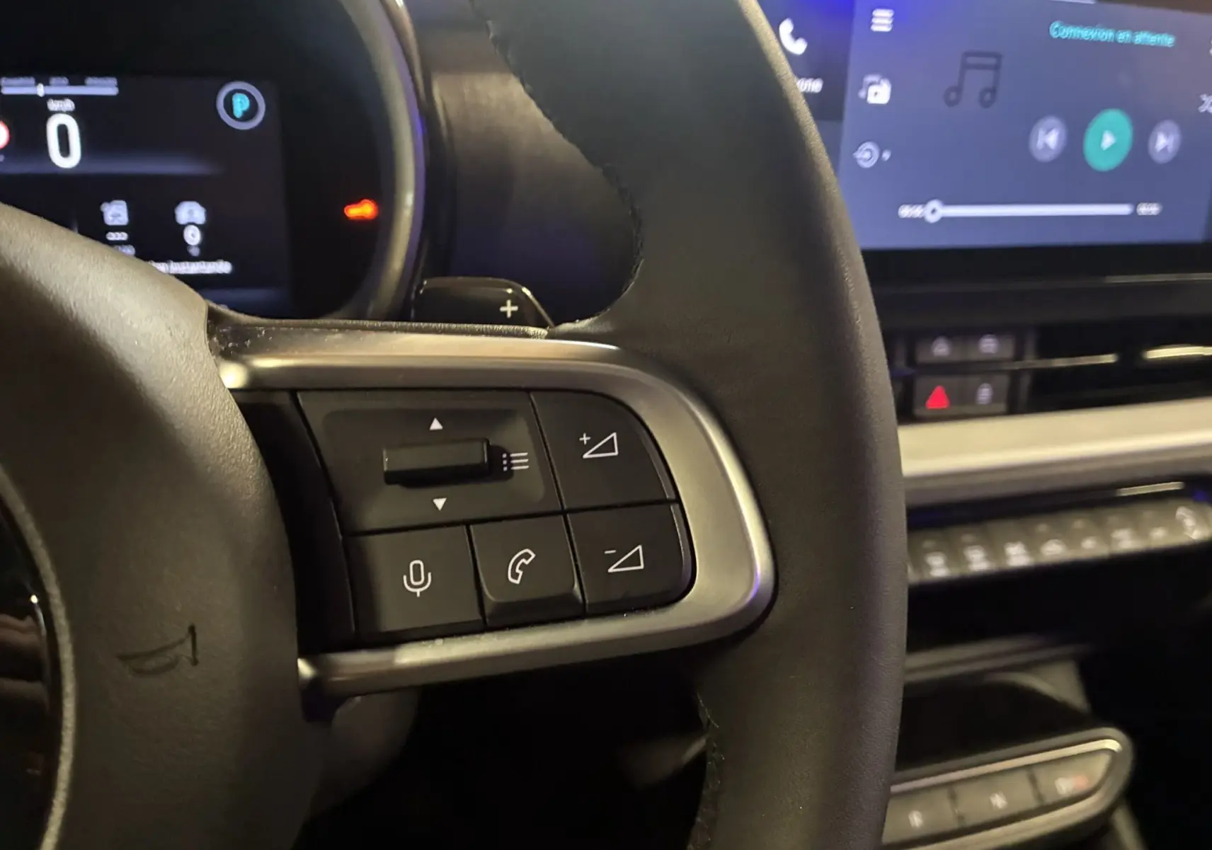 Gros plan sur les commandes au volant d'une FIAT 600 1.2 HYBRID 100 rouge, avec tableau de bord et écran tactile en arrière-plan.