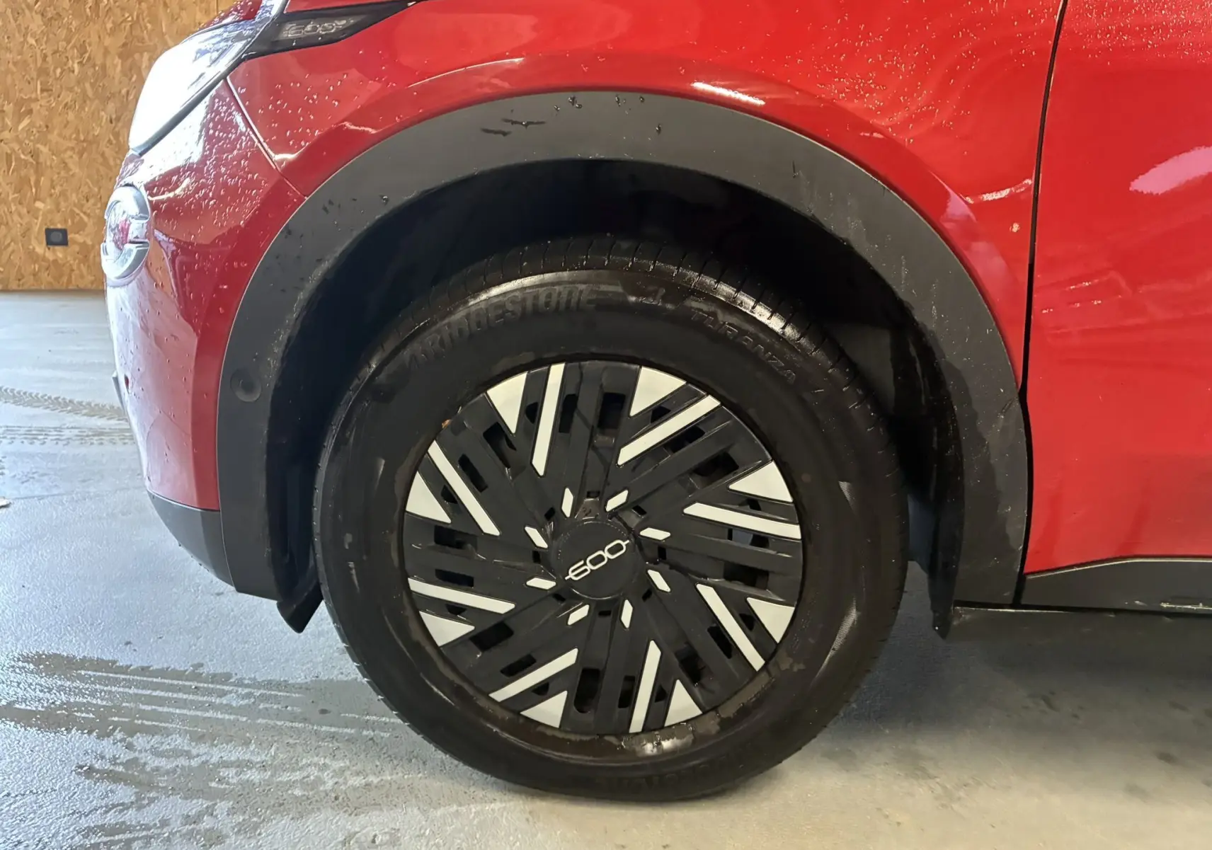 Gros plan sur la roue avant gauche d'une FIAT 600 rouge 2024, mettant en valeur la jante noire et argentée au design moderne.