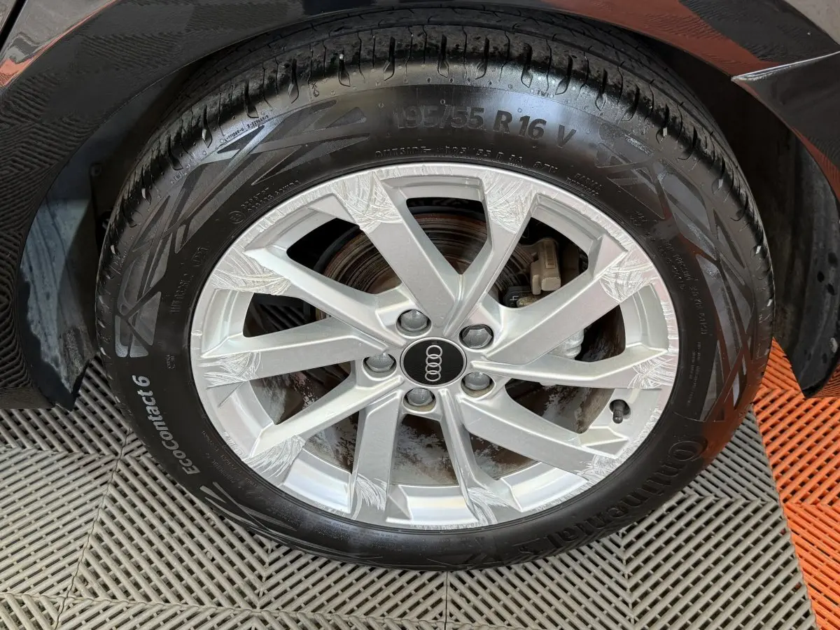 Gros plan sur la roue avant droite d'une Audi A1 noire, jante alliage argent avec logo Audi au centre.