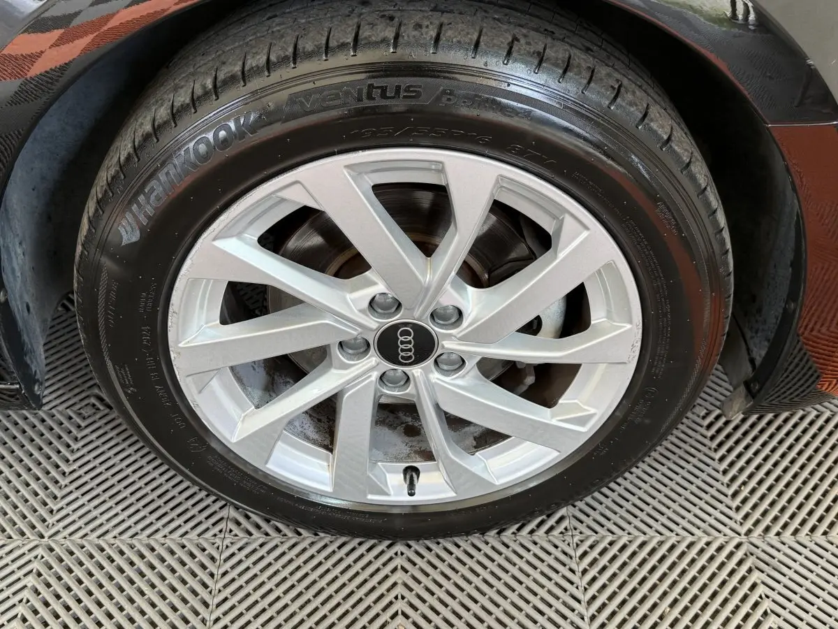 Gros plan sur la jante argentée avec logo Audi d'une Audi A1 noire, vue côté roue avant droite.