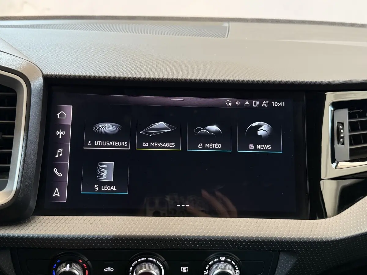 Écran tactile central de l’Audi A1 2021 affichant les menus messages, météo, news et utilisateurs, intérieur noir.