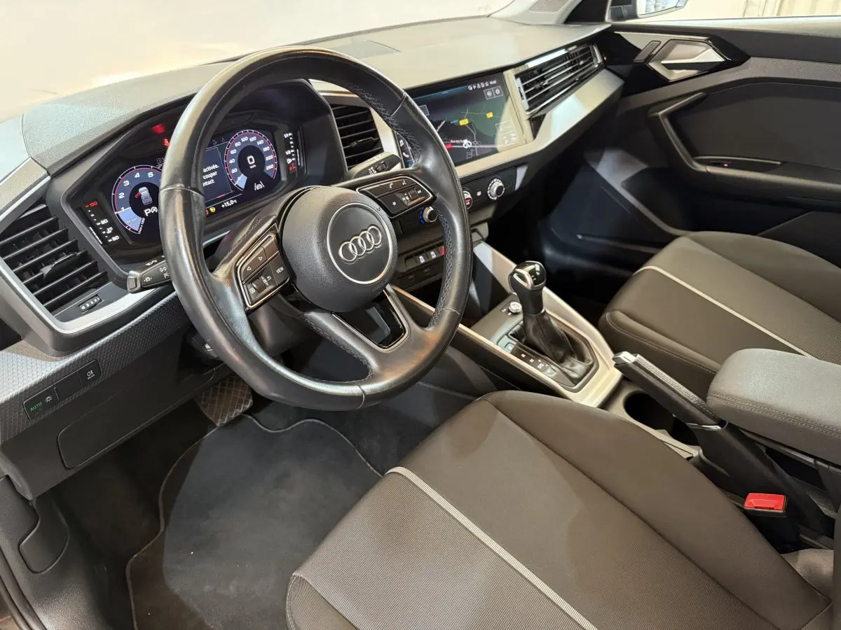 Vue intérieure côté conducteur de l'Audi A1 2021 noir, volant cuir multifonctions et tableau de bord digital.