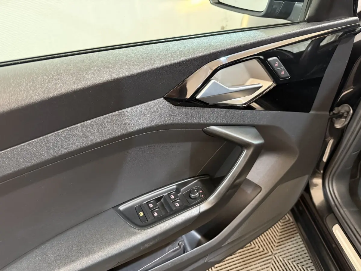 Intérieur côté conducteur de l'Audi A1 noir, montrant la porte avec commandes des vitres et poignée argentée.