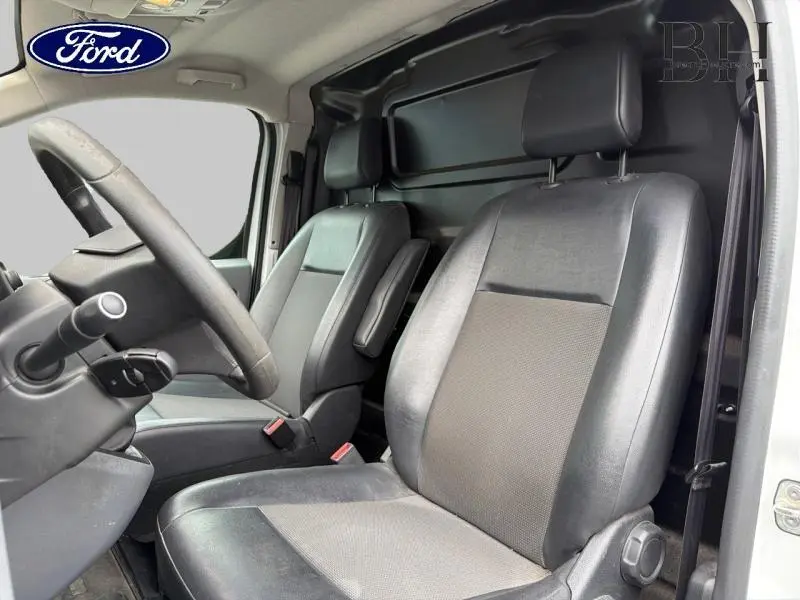 Vue intérieure côté conducteur du Peugeot Expert Fourgon blanc, montrant les sièges avant en tissu noir-gris et accoudoir passager.