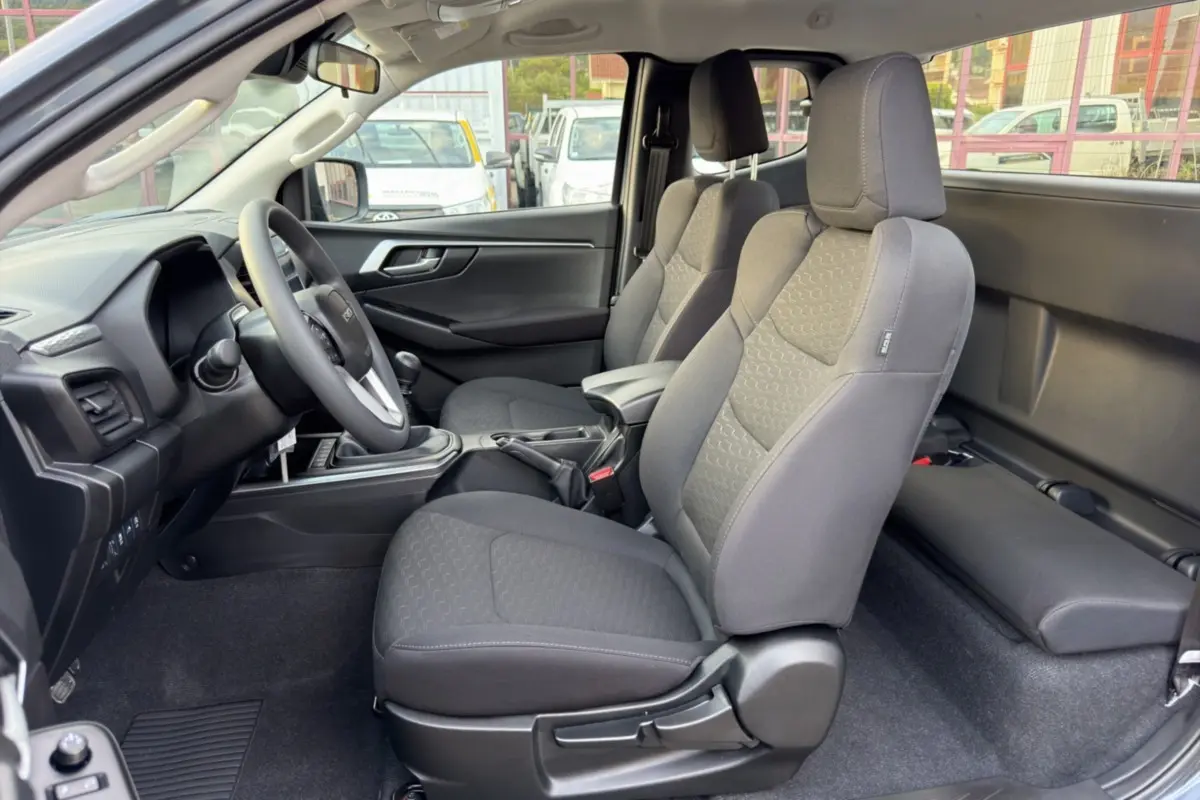Vue intérieure côté conducteur de l'Isuzu D-MAX 2026, sièges tissu gris avec accoudoir central avant.