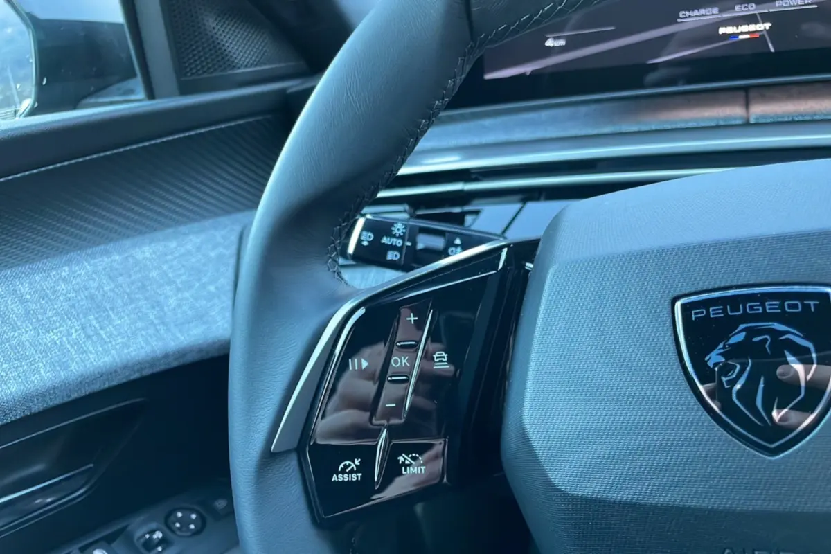 Gros plan sur le volant cuir multifonctions gris avec logo Peugeot et commandes d’assistance visibles côté gauche.