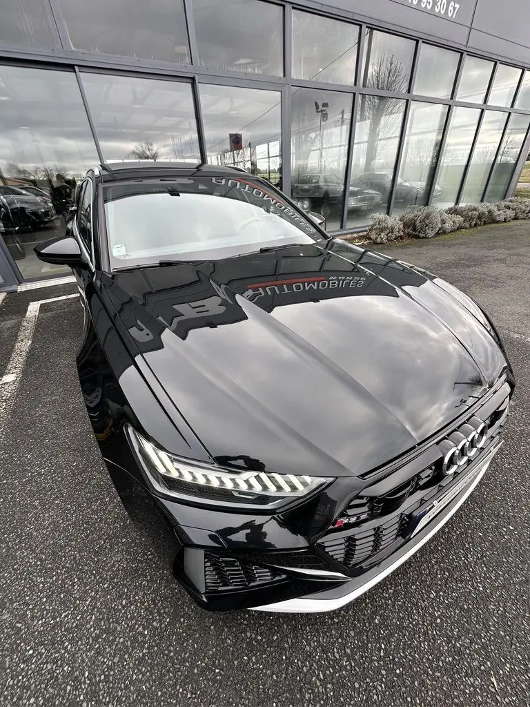 Audi RS6 Avant noir vue 3/4 avant droit, phares LED allumés et calandre sport avec logo RS6 visible.