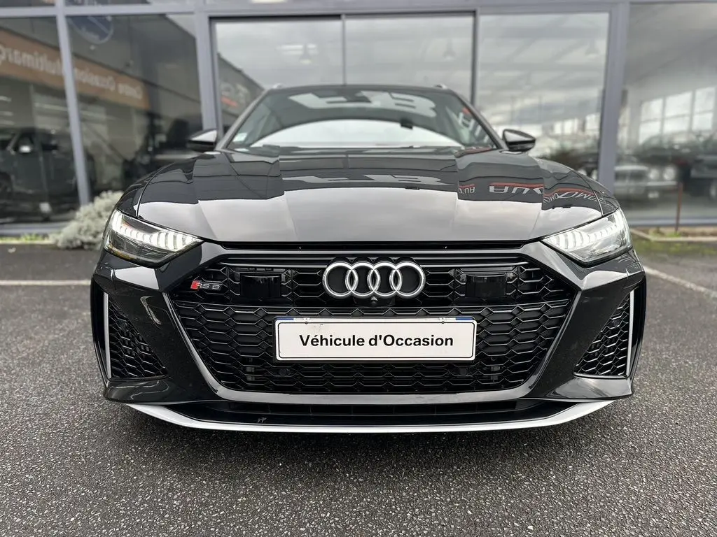 Vue frontale d'une Audi RS6 Avant noire 2021 avec calandre hexagonale et phares LED allumés.