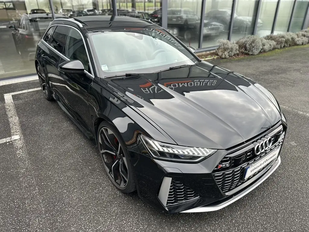 Audi RS6 Avant noir vue 3/4 avant droit, avec calandre distinctive et jantes sportives noires et rouges.