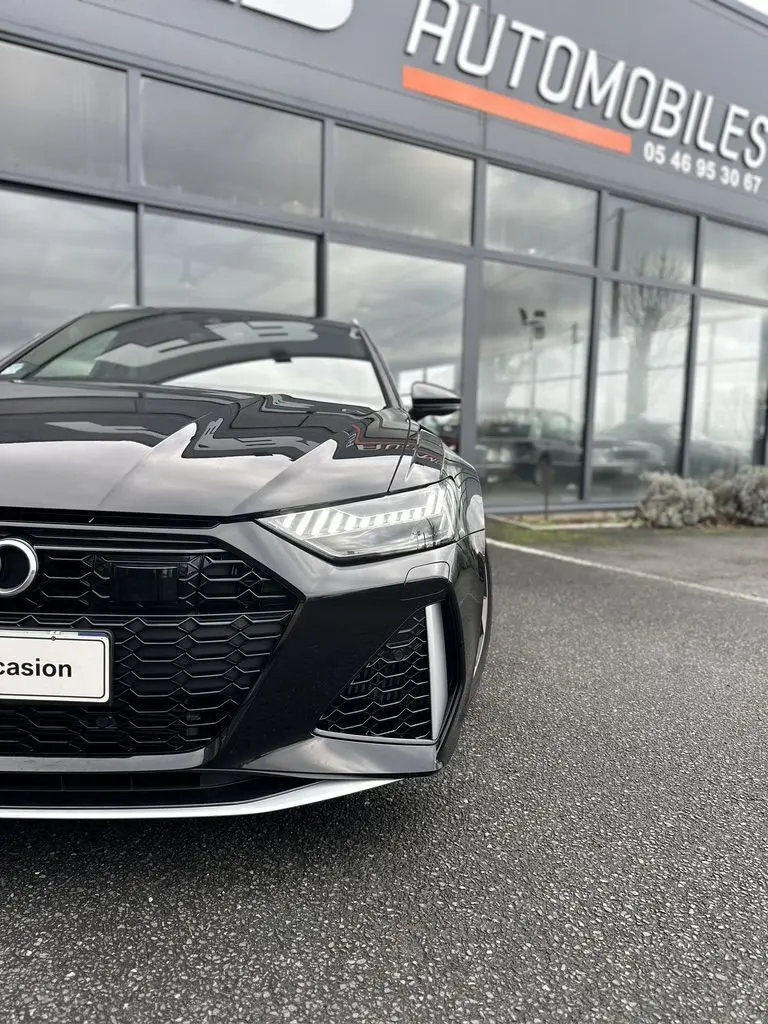 Vue de face rapprochée d'une Audi RS6 Avant noire 2021 avec calandre hexagonale et phares LED allumés.