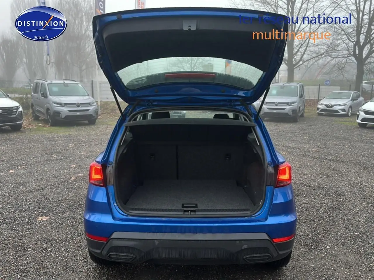 Vue arrière d’un SEAT Arona bleu saphir avec hayon ouvert montrant le coffre vide sur un parking extérieur.