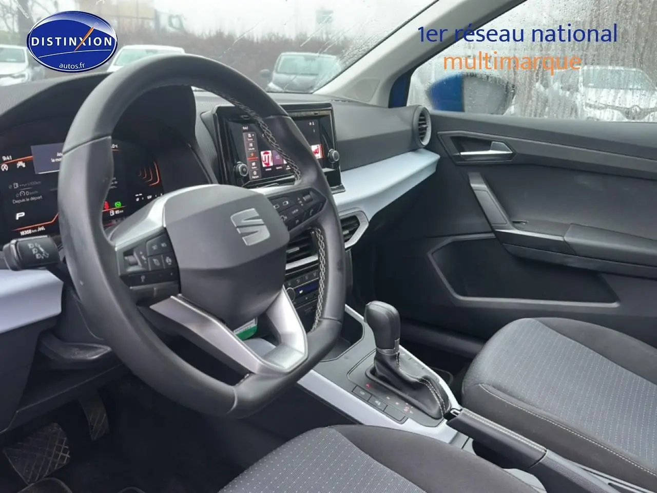 Intérieur avant droit du SEAT Arona 2025, volant cuir méplat, console centrale avec écran tactile et sellerie tissu gris.