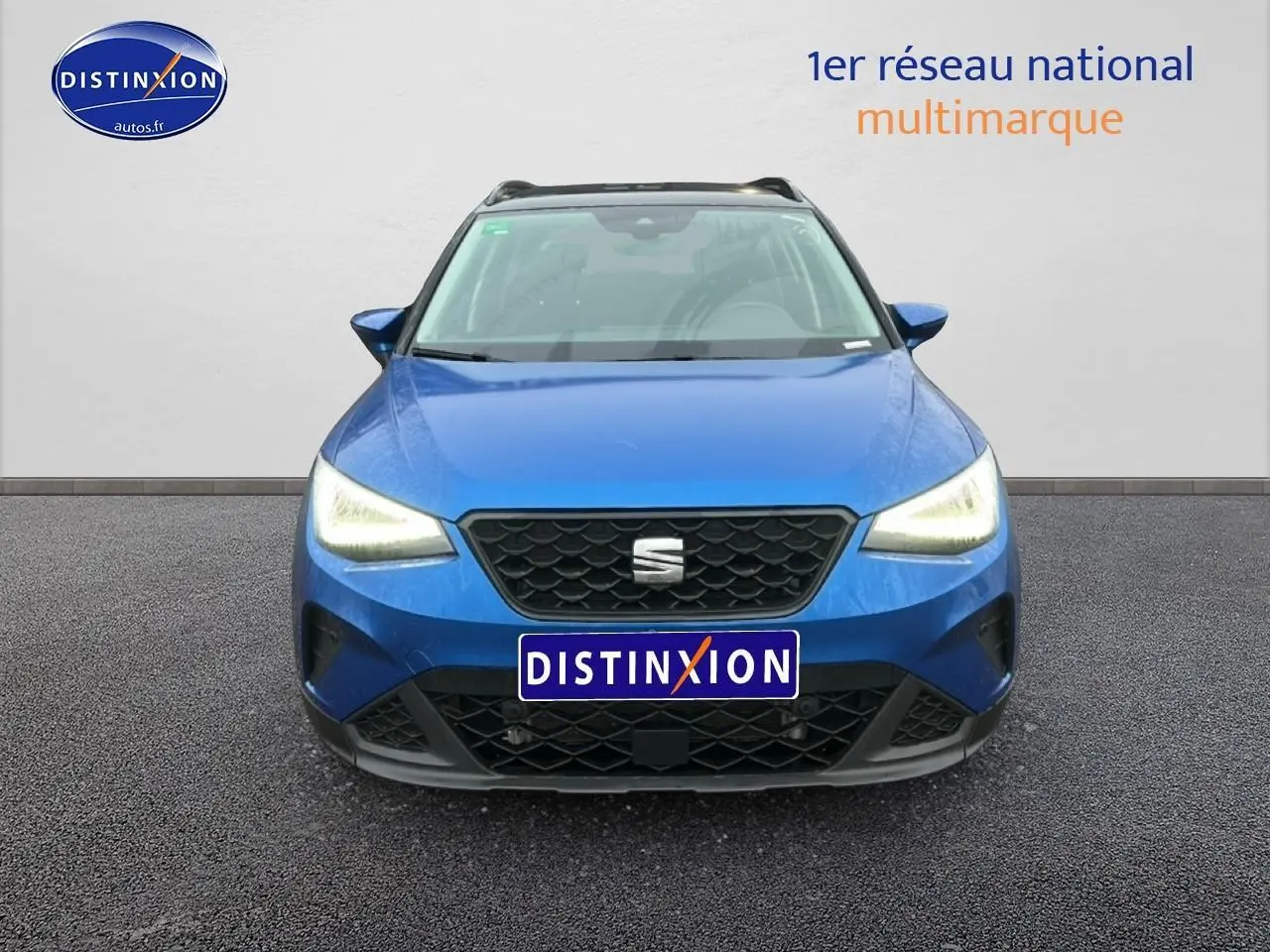 Vue frontale d'un SEAT Arona bleu saphir avec phares allumés et calandre noire au logo central.