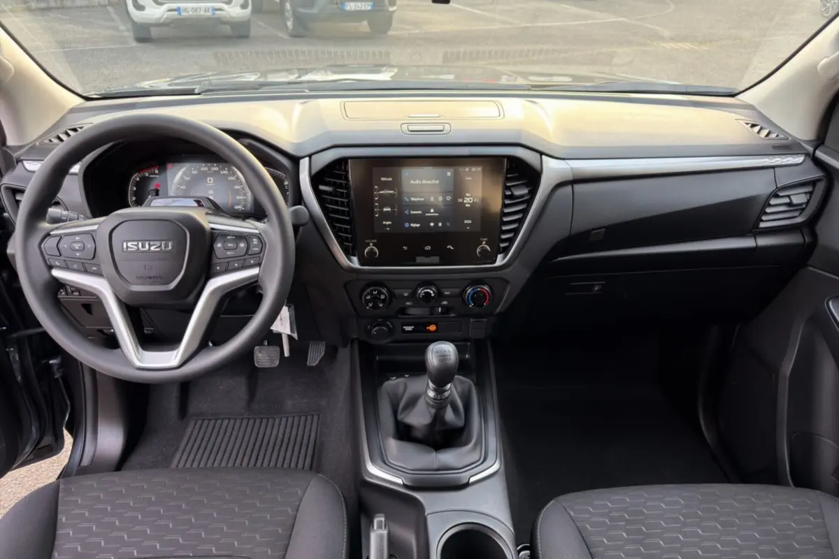 Vue intérieure avant de l'Isuzu D-MAX 2026 avec tableau de bord noir et écran tactile central allumé.