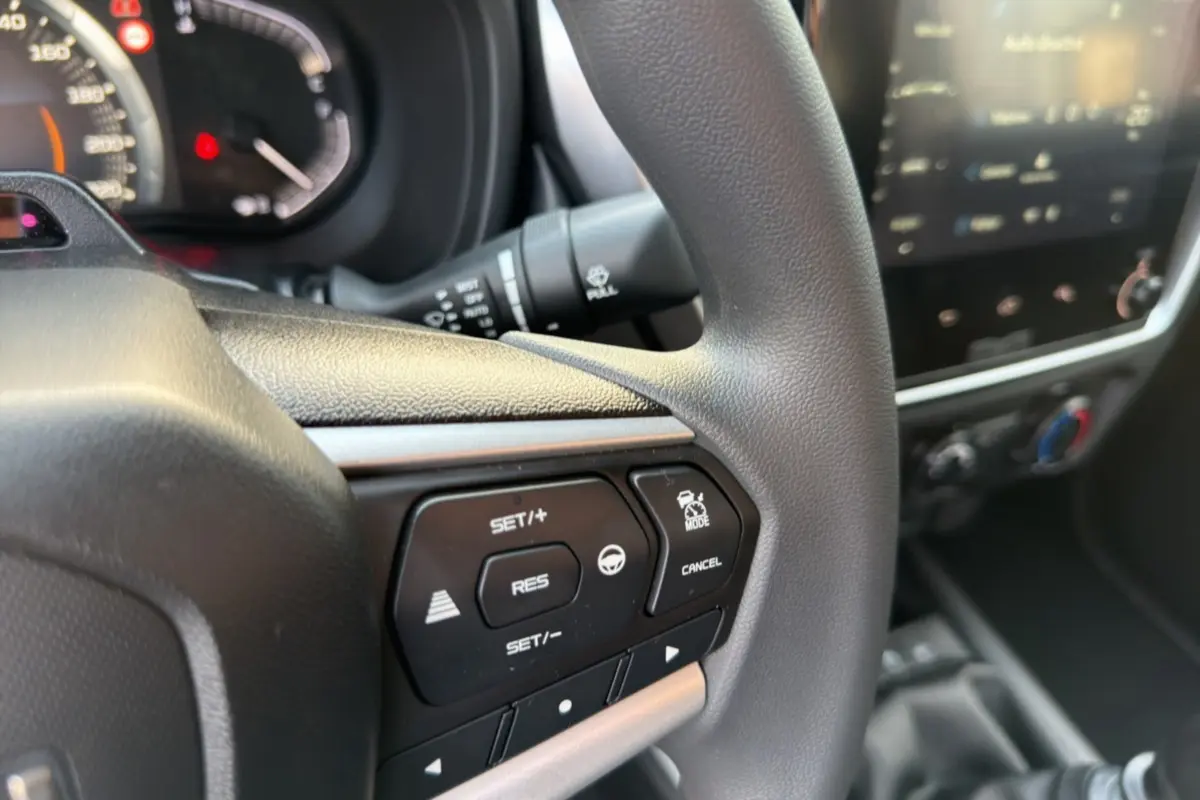 Gros plan sur le volant multifonctions noir de l'Isuzu D-MAX 2026 avec commandes de régulateur et tableau de bord flou.