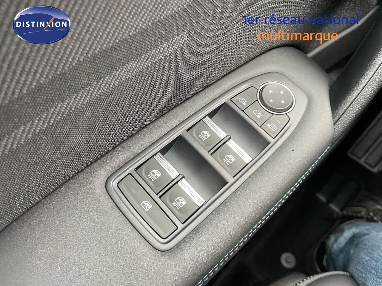 Gros plan sur les commandes de lève-vitres côté gauche avec surpiqûres bleues dans l’habitacle noir du Renault Symbioz gris Rafale.