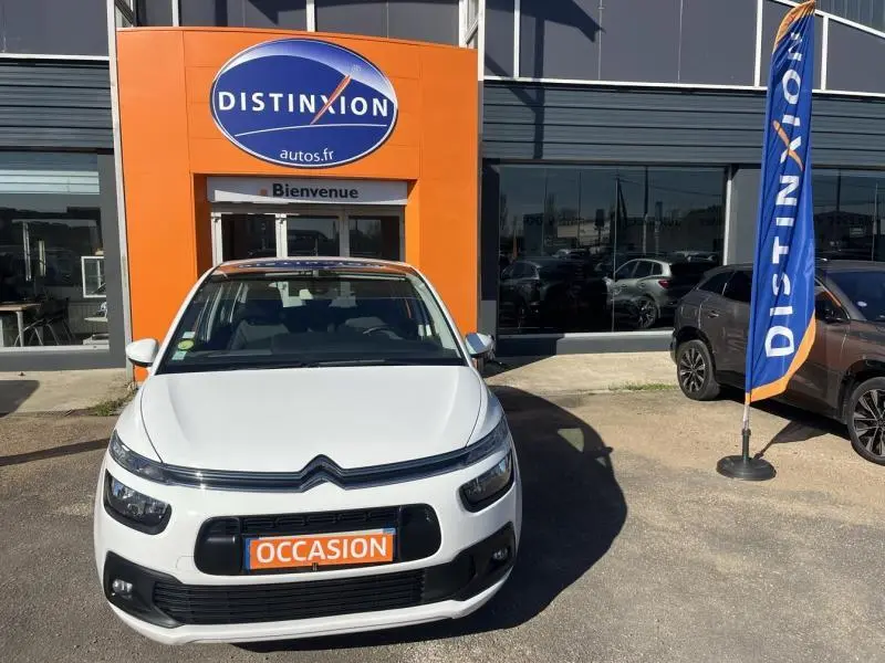 Vue avant d'un Citroën Grand C4 Spacetourer blanc Banquise avec plaque "OCCASION" devant un concessionnaire Distinxion.