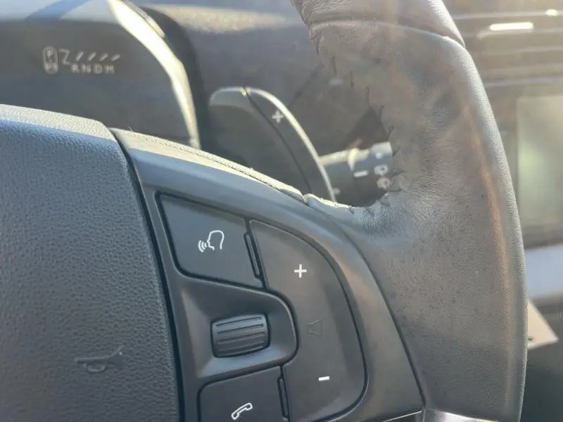Gros plan sur les commandes vocales et volume au volant cuir du Citroën Grand C4 Spacetourer blanc Banquise, intérieur lumineux.