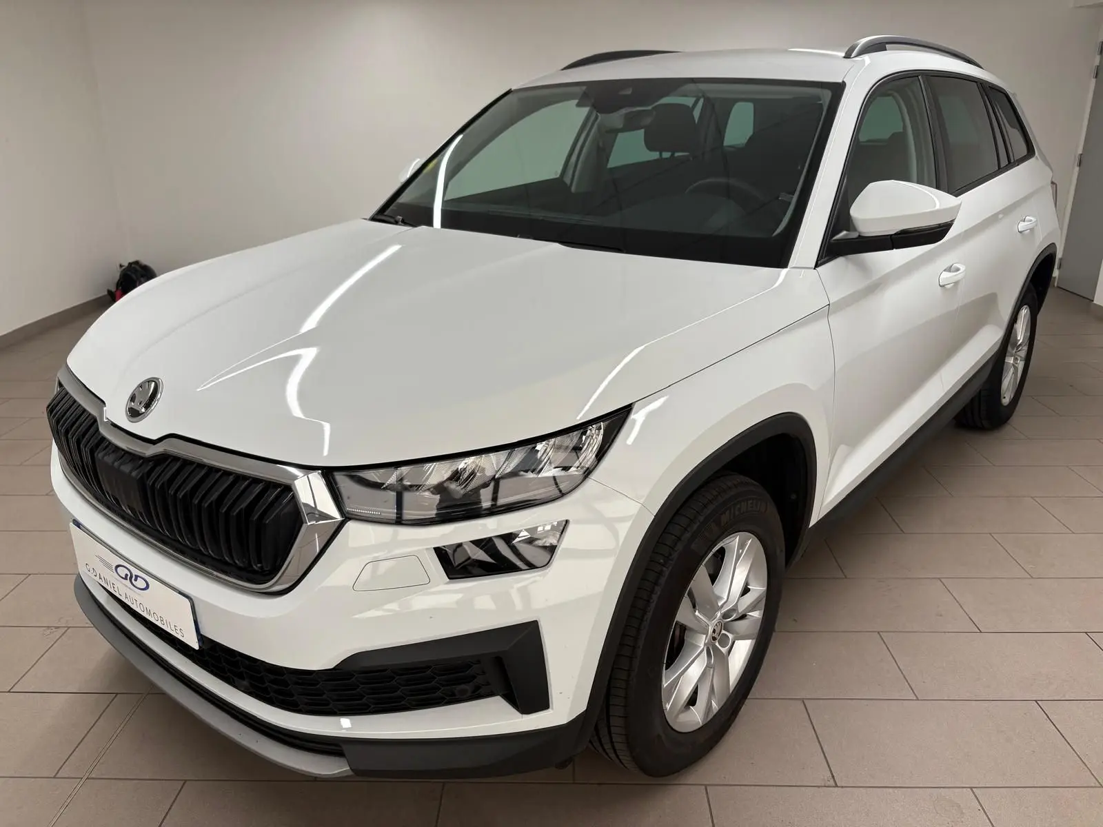 SKODA KODIAQ blanc lune vu en 3/4 avant droit dans un intérieur, avec calandre noire et jantes argentées.
