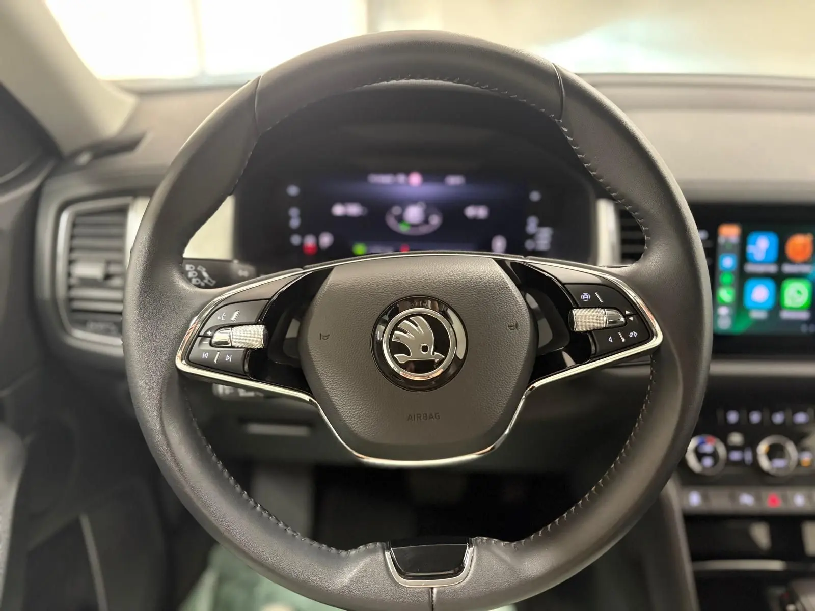 Gros plan sur le volant cuir noir du Skoda Kodiaq avec logo central et tableau de bord digital en arrière-plan.