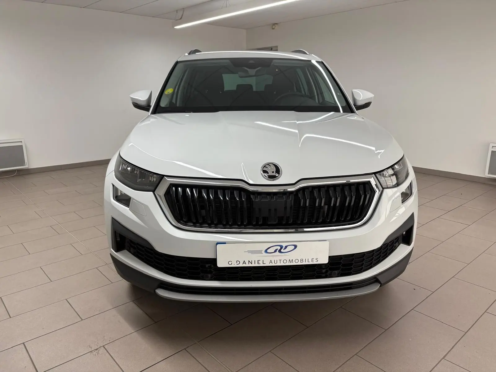 Vue frontale d'un Skoda Kodiaq blanc Lune 2022 avec calandre noire et logo au centre dans un showroom.