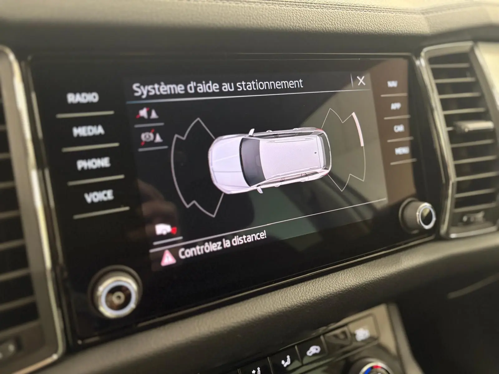 Écran central du Skoda Kodiaq blanc lune montrant le système d'aide au stationnement en vue du dessus.