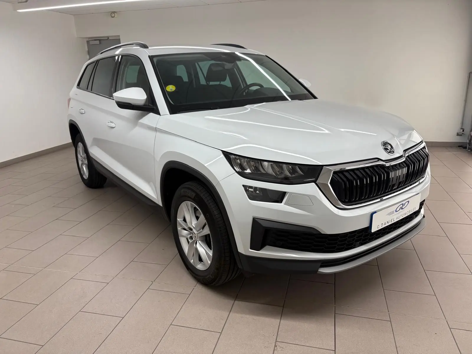 Vue 3/4 avant d'un Skoda Kodiaq blanc lune 2022 en intérieur, avec calandre noire et jantes argentées.