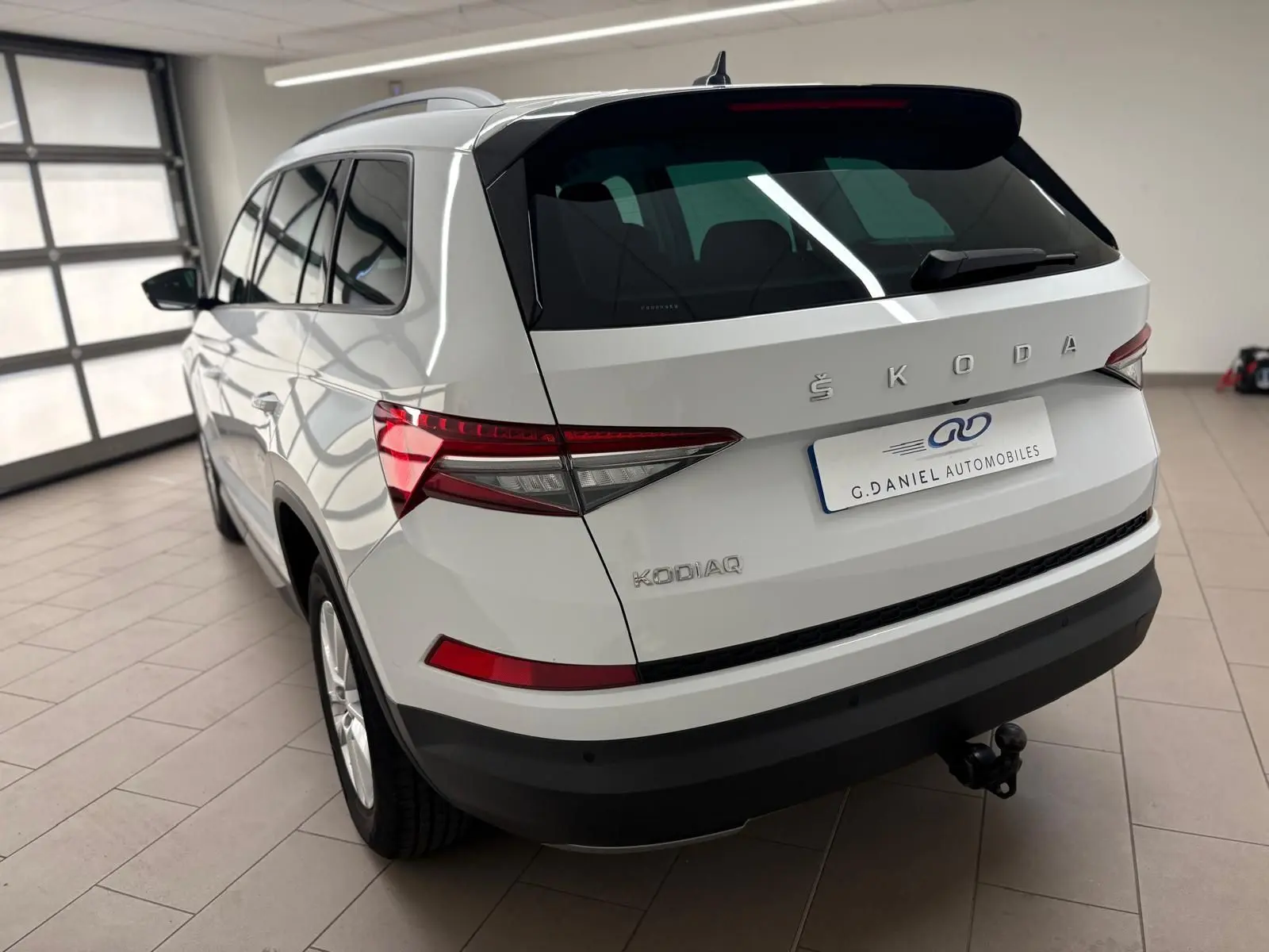 Vue 3/4 arrière droite d'un Skoda Kodiaq blanc Lune 2022 avec crochet d'attelage escamotable en intérieur showroom.