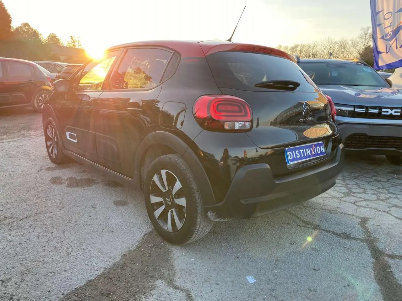 Vue 3/4 arrière gauche d'une Citroën C3 2023 noire avec toit rouge et jantes alliage diamantées au soleil couchant.